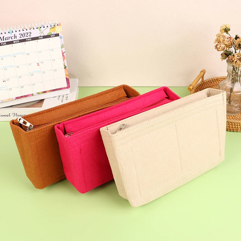 A set of felt cosmetic bag insert organizers in shades of orange, pink, and beige are displayed next to a calendar.
