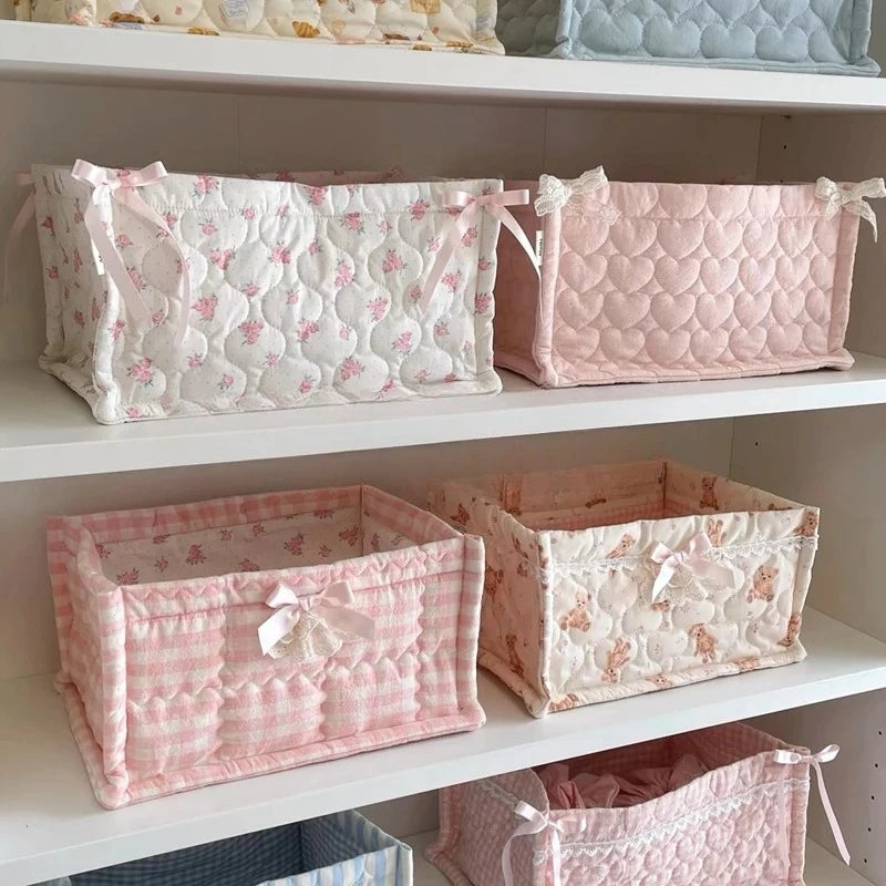 Pink and white quilted cotton storage baskets with lace flower designs displayed on white shelves.