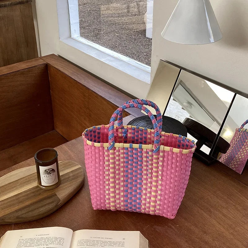 A pink and blue hand woven PVC vegetable basket tote bag sitting on a wooden table.