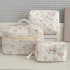 A white quilted cosmetic bag with pink ribbon details is displayed on a white surface.