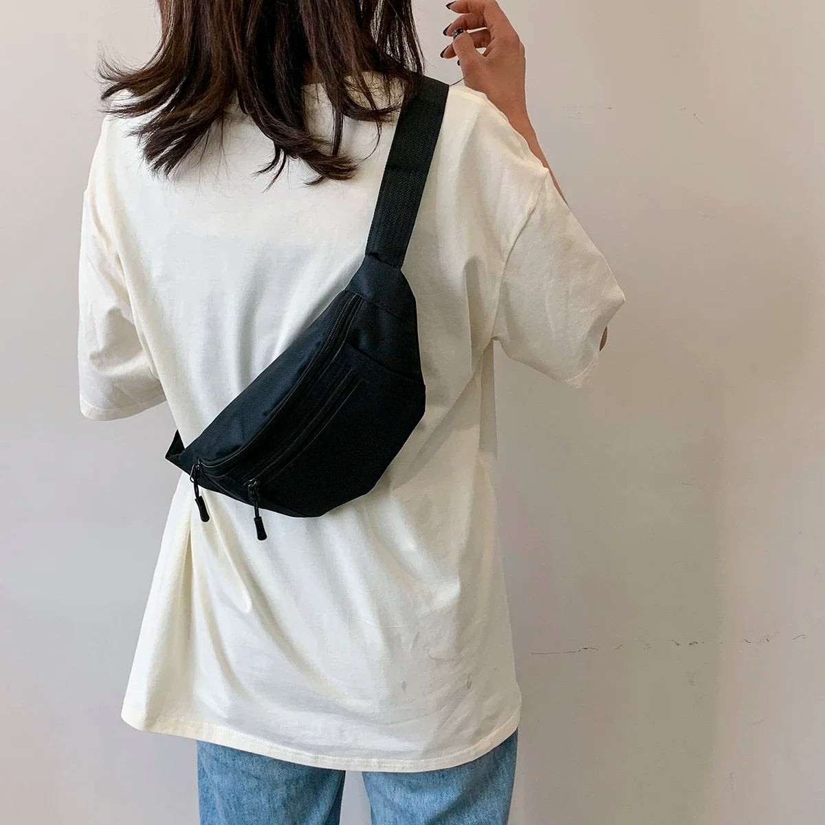 A woman wearing a white shirt and jeans is holding a black compact nylon waist bag.