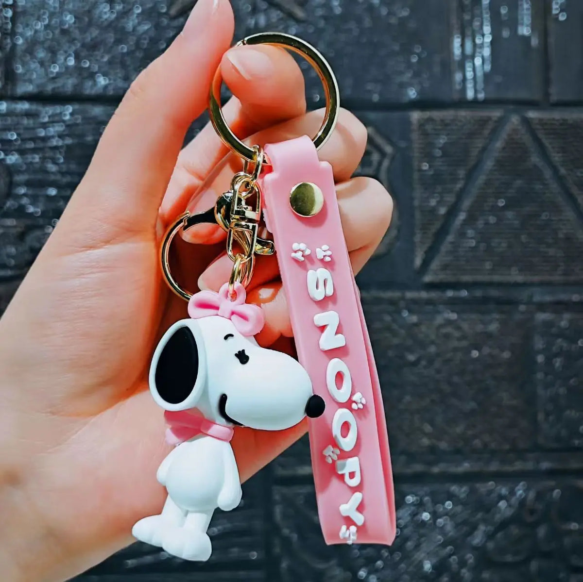 A hand holds a pink silicone keychain featuring a white Snoopy character.
