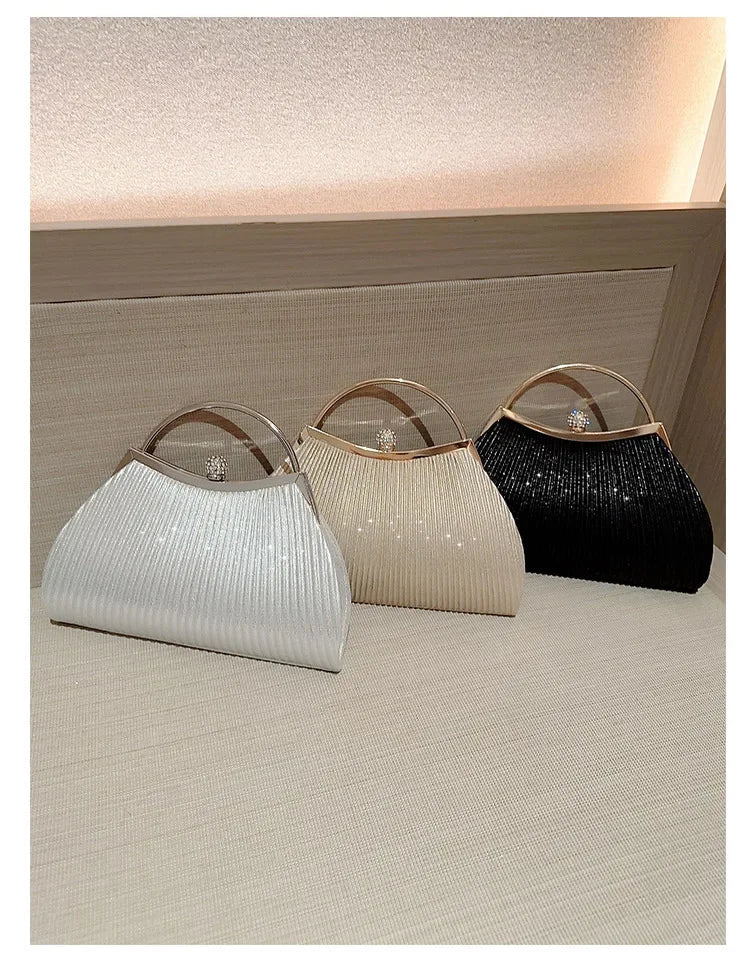 Three pleated glitter evening handbags in white, beige, and black displayed on a light surface.