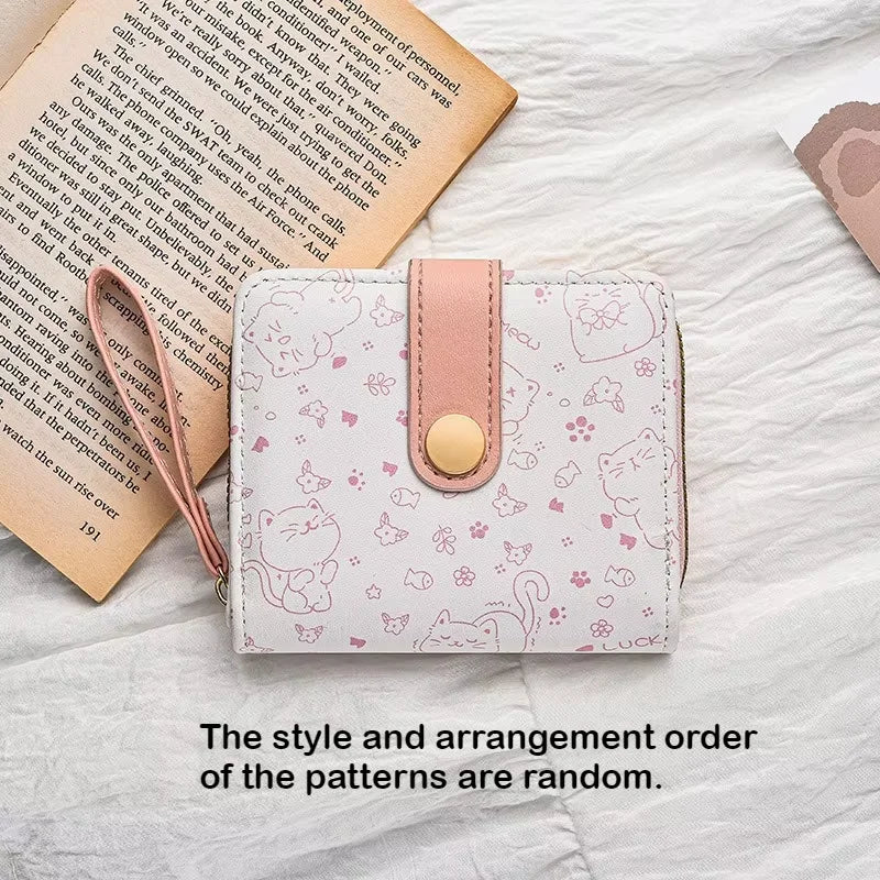A pink and white patterned cat cartoon coin purse and card holder wallet resting on a white surface next to an open book.