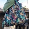 A dark patterned canvas tote shopping bag is shown being carried by a person outdoors.