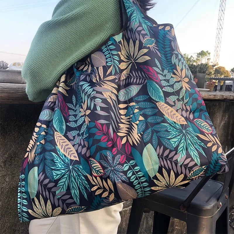 A dark patterned canvas tote shopping bag is shown being carried by a person outdoors.