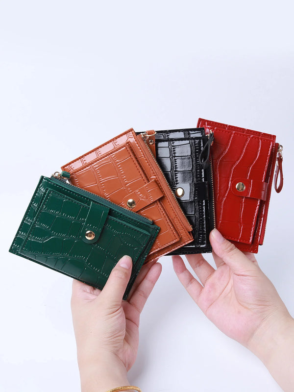 A hand holds four mini leather card holders in shades of brown, black, and red with crocodile patterns.