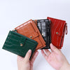 A hand holds four mini leather card holders in shades of brown, black, and red with crocodile patterns.