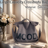 A gray crossbody bag made of sailcloth with the word MOOD printed on it, displayed next to roses and books.