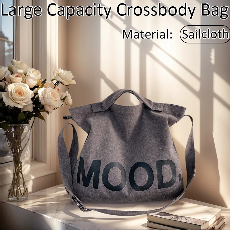 A gray crossbody bag made of sailcloth with the word MOOD printed on it, displayed next to roses and books.