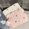 A pink quilted slim laptop sleeve with black bow embroidery is shown against a window background.