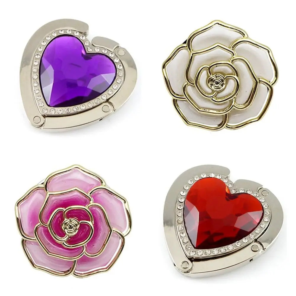 A set of three heart-shaped metal foldable bag hooks featuring purple, white, and red gemstone accents.