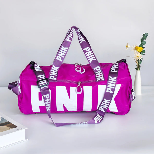 A bright purple Nike pink shoulder bag with white text is displayed on a white surface next to a small vase of yellow flowers