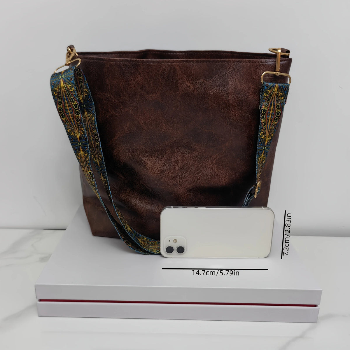 A dark brown leather geometric strap crossbody hobo bag resting on a white box.