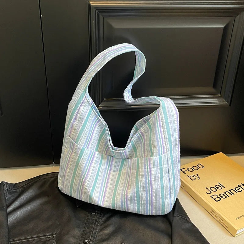 A light blue and white striped canvas shoulder bag is displayed on a black leather jacket.
