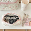 Sac de rangement cosmétique blanc avec motif nœud rose, à côté d'une tasse rose et de pinceaux de maquillage.