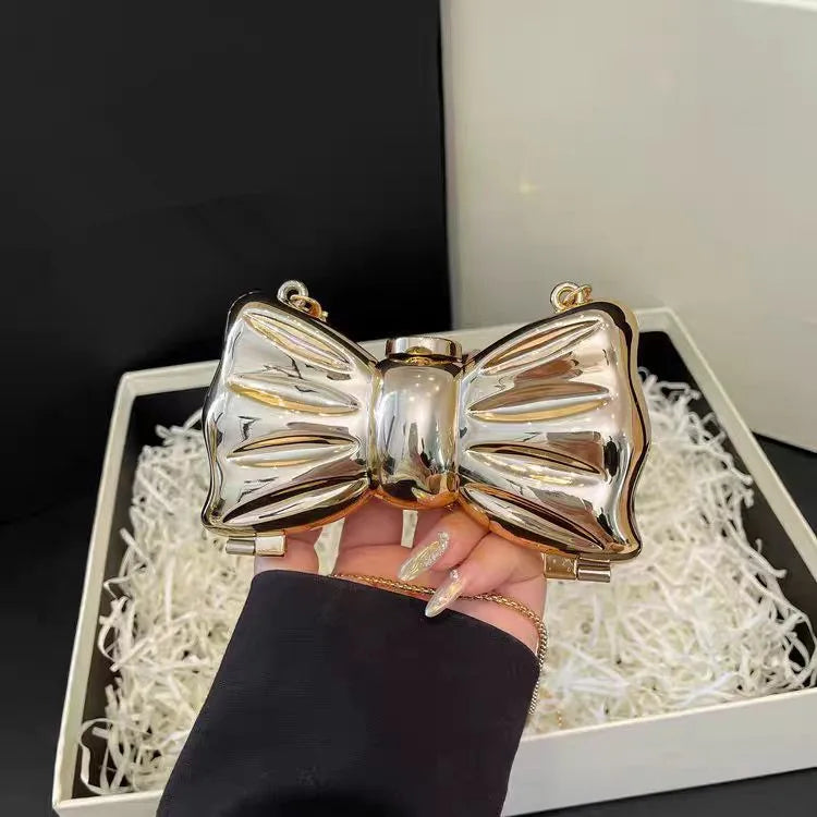 A hand holds a heart-shaped gold-toned acrylic evening clutch with a chain strap, resting on white shredded material.