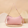 A pink leather shoulder bag with a gold chain pendant resting on a woven mat.