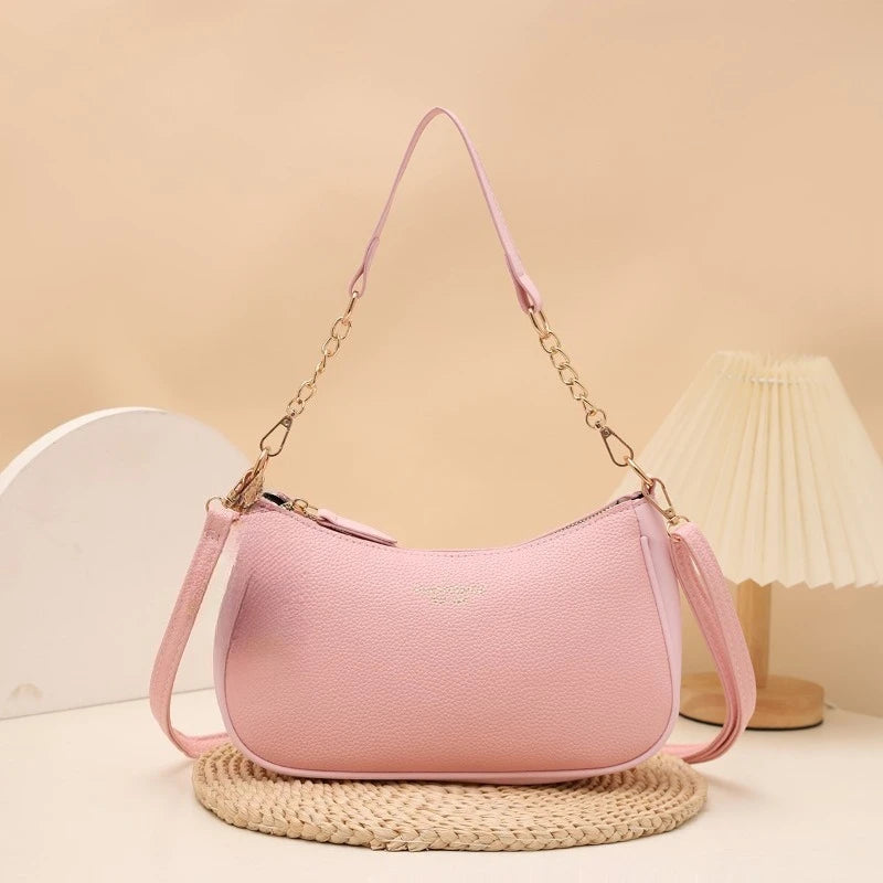 A pink leather shoulder bag with a gold chain pendant resting on a woven mat.