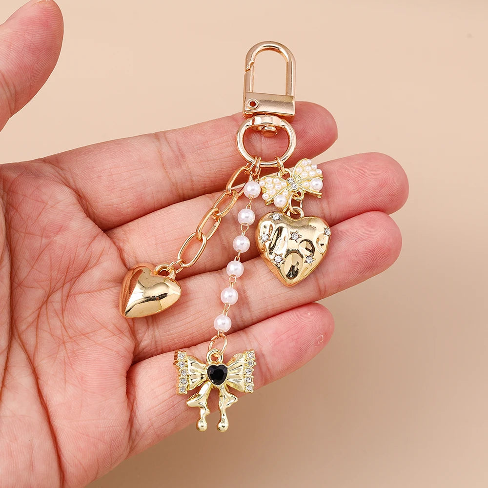A gold-toned pearl bow heart keychain is held in a hand against a neutral background.