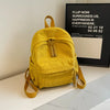 A yellow corduroy daily backpack is displayed on a white surface next to a framed sign.