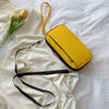 A yellow multi-pocket waterproof travel document organizer rests on white fabric with a black strap and a glass of tulips.