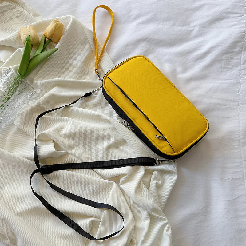 A yellow multi-pocket waterproof travel document organizer rests on white fabric with a black strap and a glass of tulips.