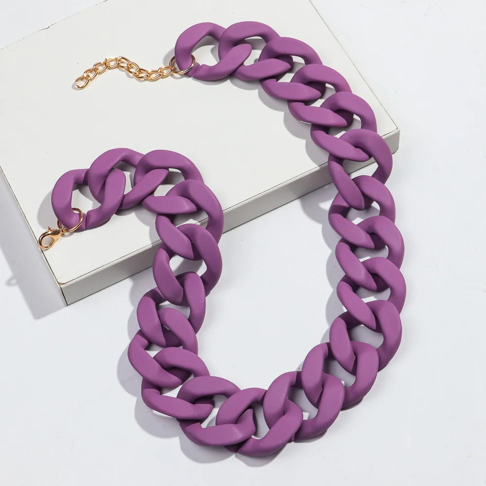 A purple matte acrylic chain necklace with a gold-colored clasp is displayed on a white box.