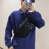 Eine Person in einem königsblauen Langarmshirt hält eine schwarz karierte Brusttasche und macht ein Foto mit einem Smartphone