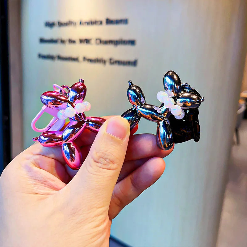 A hand holds a shiny, metallic purple and pink balloon dog keychain charm against a blurred background.