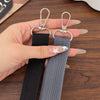 A hand holds an adjustable wide shoulder strap for bags or cameras, featuring silver clasps and black and gray fabric.