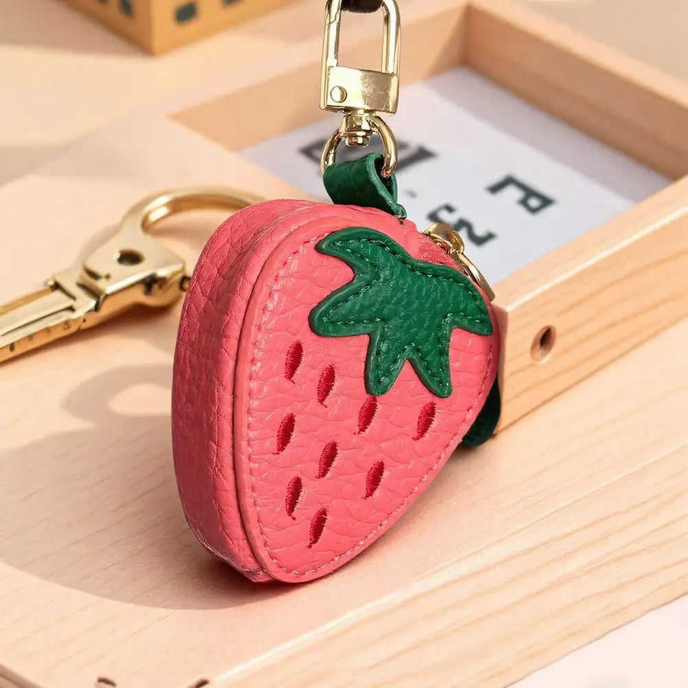 Pinkes Erdbeerkörbchen-Charm-Geldbörsen-Anhänger an einem goldfarbenen Schlüsselring, auf einer hellen Holzoberfläche.