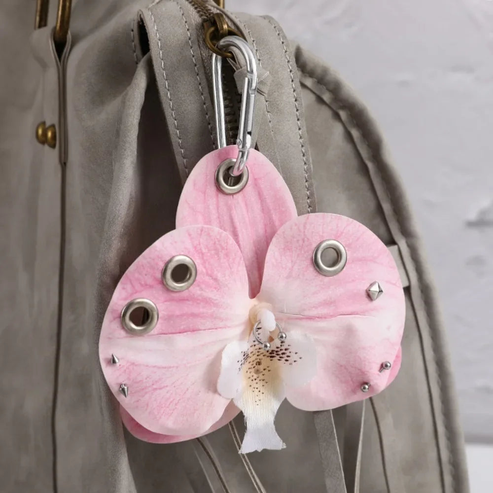 A pink orchid flower keychain attached to a gray fabric strap.