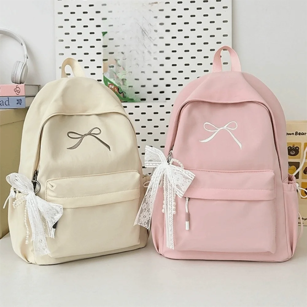 A pair of light beige and pink embroidered backpacks with white ribbon details.