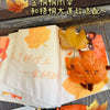 A close-up of a cute maple leaf plush charm displayed on a white fabric background with orange accents.
