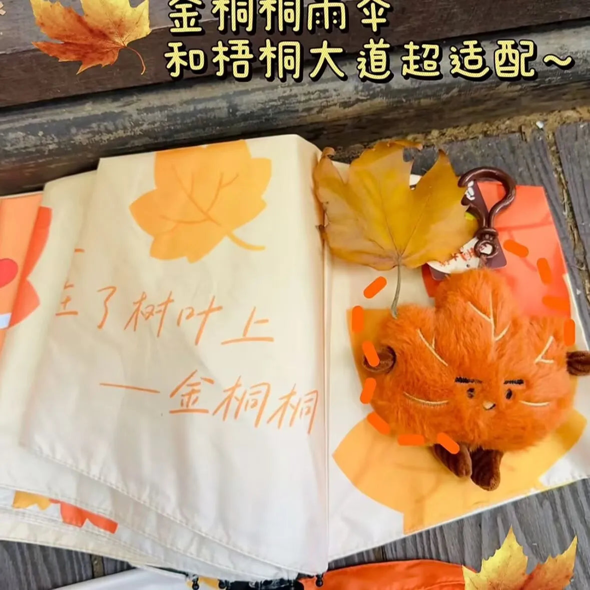 A close-up of a cute maple leaf plush charm displayed on a white fabric background with orange accents.