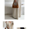 A woman models a tan faux suede crossbody bag while wearing a cream-colored dress.