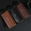 Portefeuille pochette à fermeture éclair en cuir marron pour homme, ouvert sur une surface sombre.