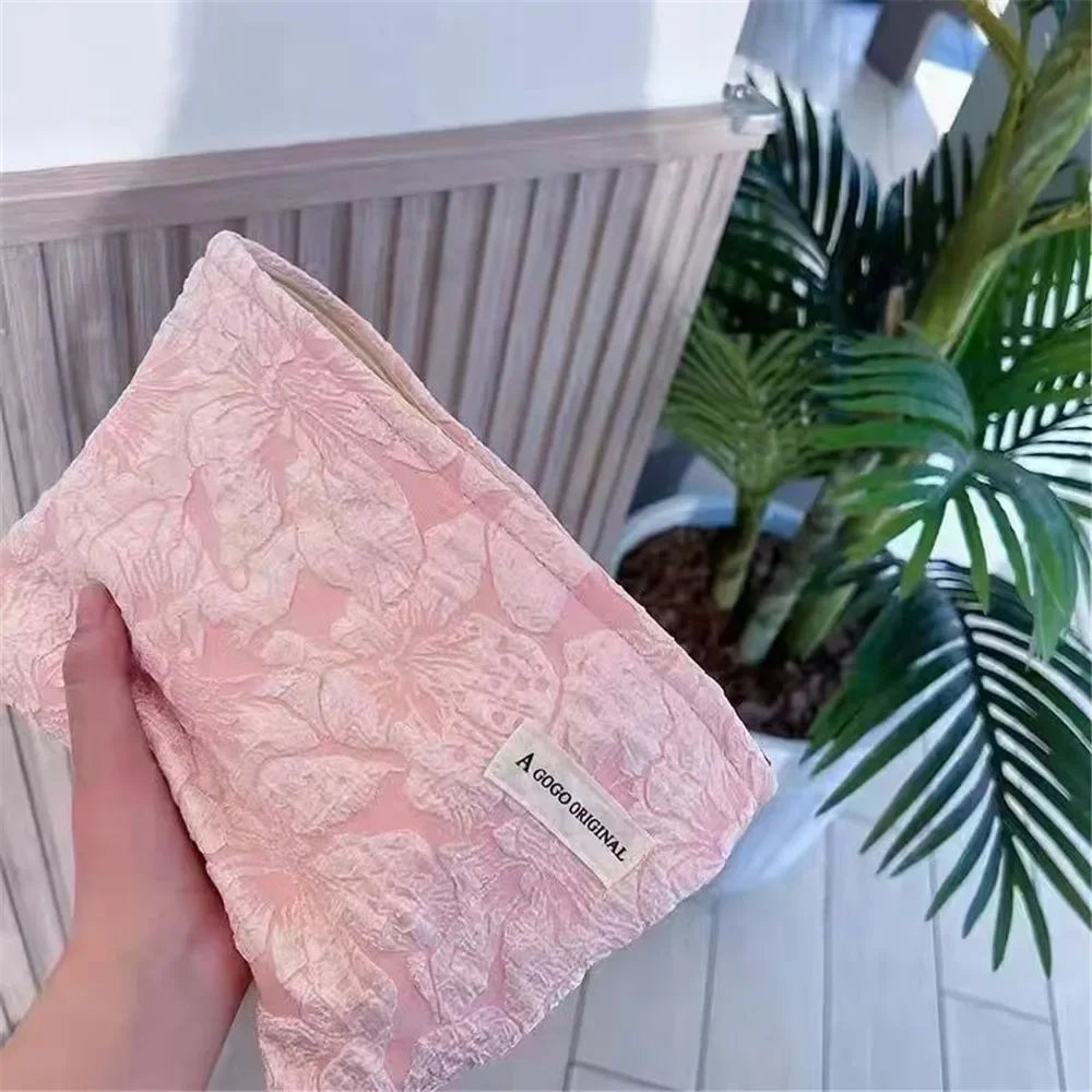 Una bolsa de almacenamiento con cremallera rosa de lona, sostenida contra un fondo de plantas tropicales verdes.