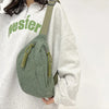 A woman wearing a light gray sweatshirt and carrying an olive green corduroy waist pack.