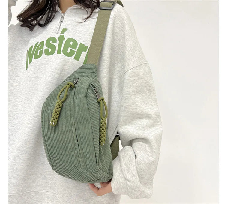 A woman wearing a light gray sweatshirt and carrying an olive green corduroy waist pack.
