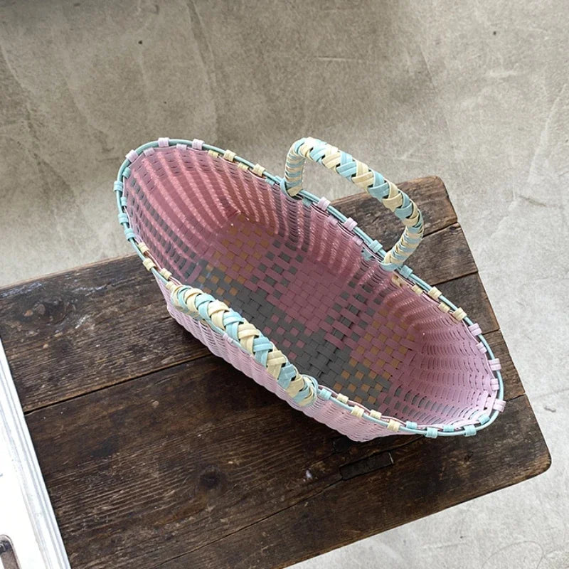 Hand woven pink and green striped PVC vegetable basket tote bag resting on a dark wooden surface.