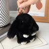 A small black plush rabbit charm with white ears is being held by a hand, displayed on a light surface.