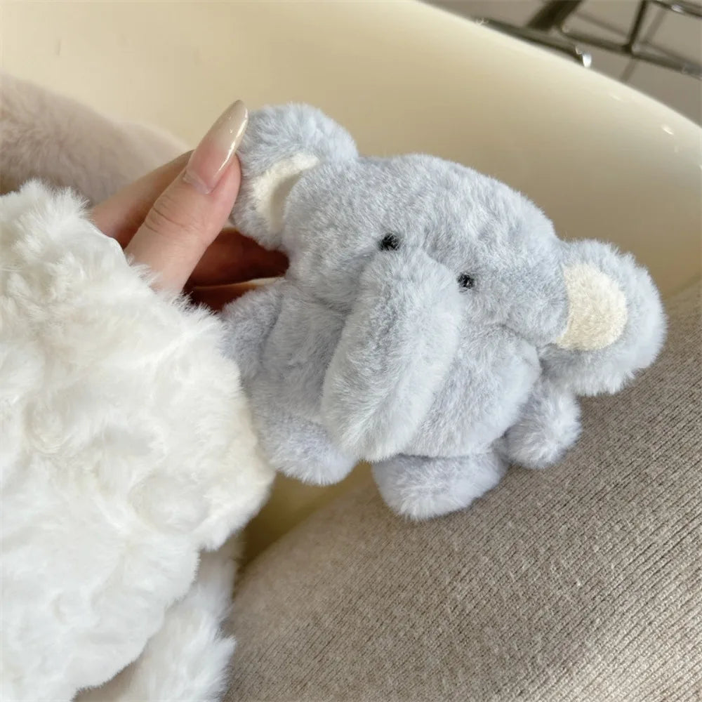 A hand is holding a small, gray plush elephant designed as an AirPods case, resting on a soft white fur fabric.
