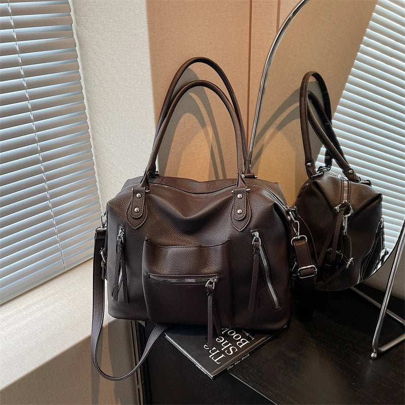 Bolso de cuero suave marrón oscuro de lujo cruzado, exhibido sobre una superficie oscura junto a un espejo.