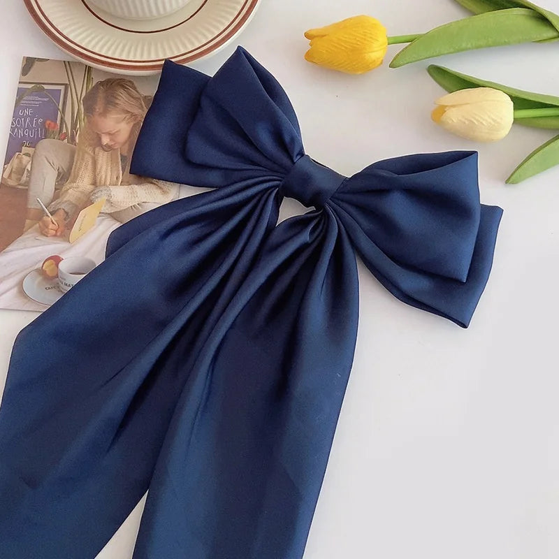 A navy blue silk bow tied in a large knot, placed next to yellow tulips and a magazine.
