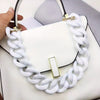 A white acrylic chunky chain shoulder strap is draped over a white handbag.
