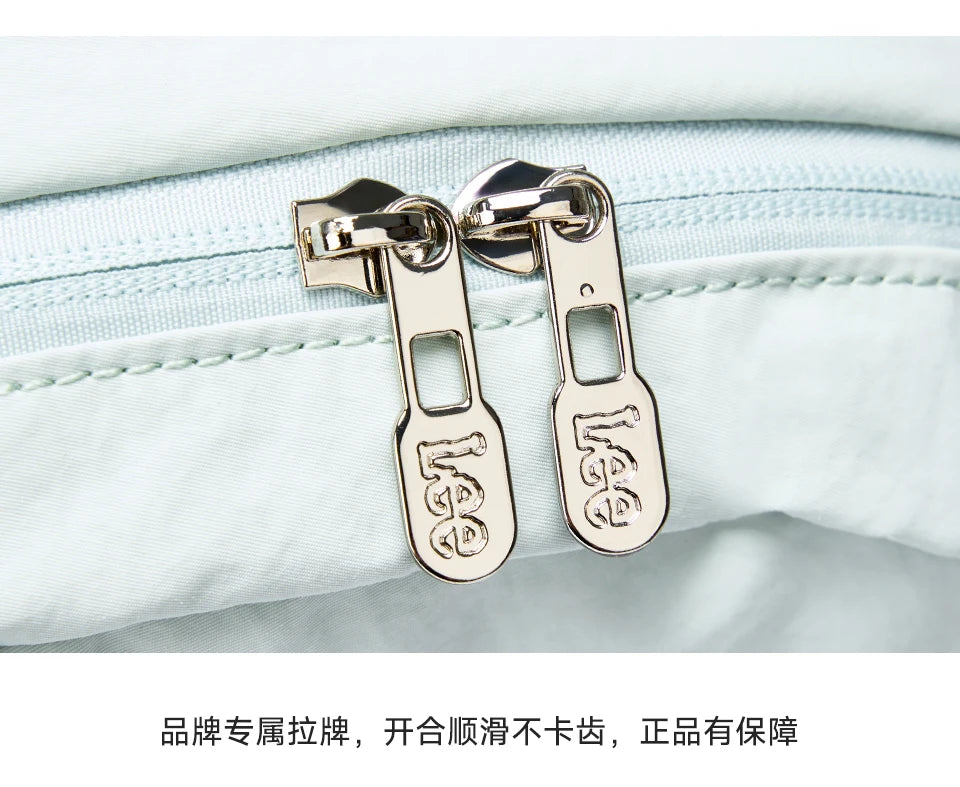 Gold-toned luggage tags attached to a light blue fabric, used for securing the lightweight waterproof daypack.