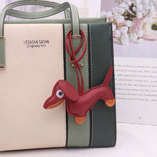 A light beige and olive green leather handbag with a red dachshund pet keychain charm.