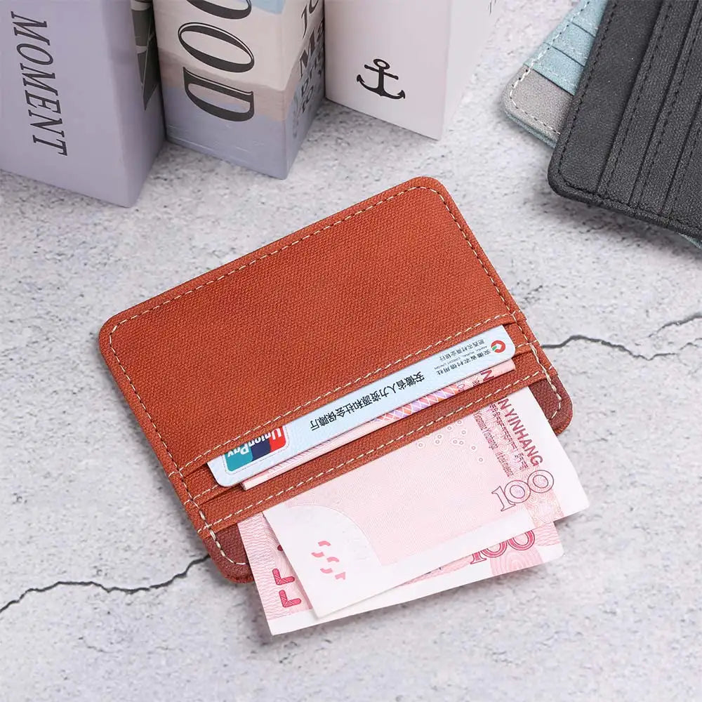 A brown PU leather card holder wallet with a keychain and several pink 100 yuan banknotes is shown on a light surface.